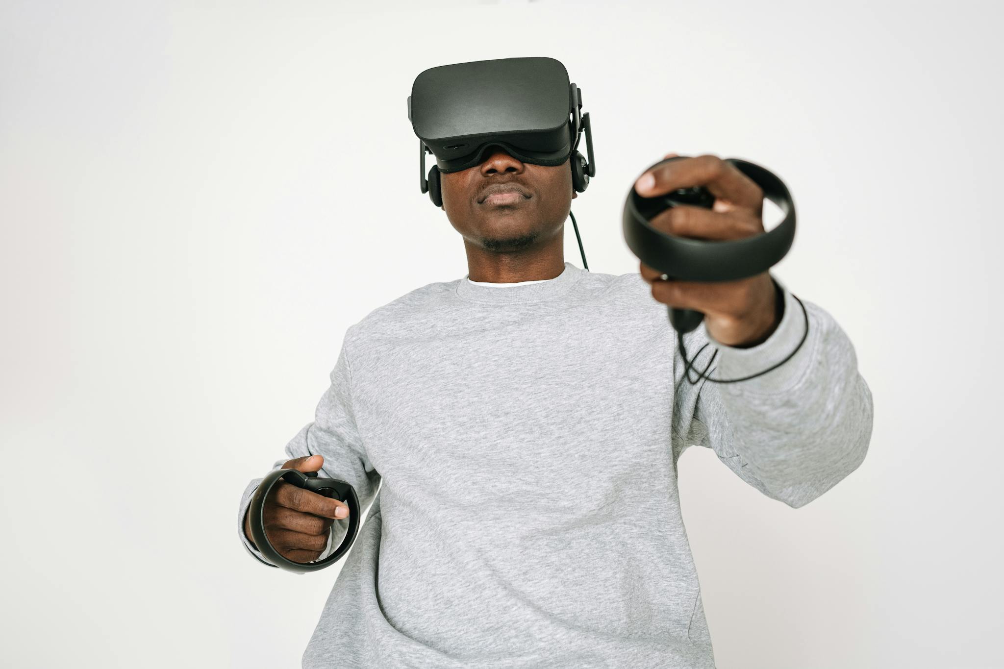 Adult man in gray sweater using VR headset and controllers, immersed in virtual reality gaming.