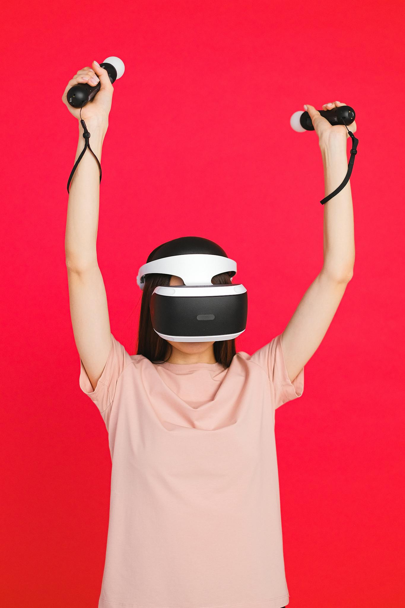 Young adult woman using a virtual reality headset while holding controllers, standing against a vibrant red backdrop.